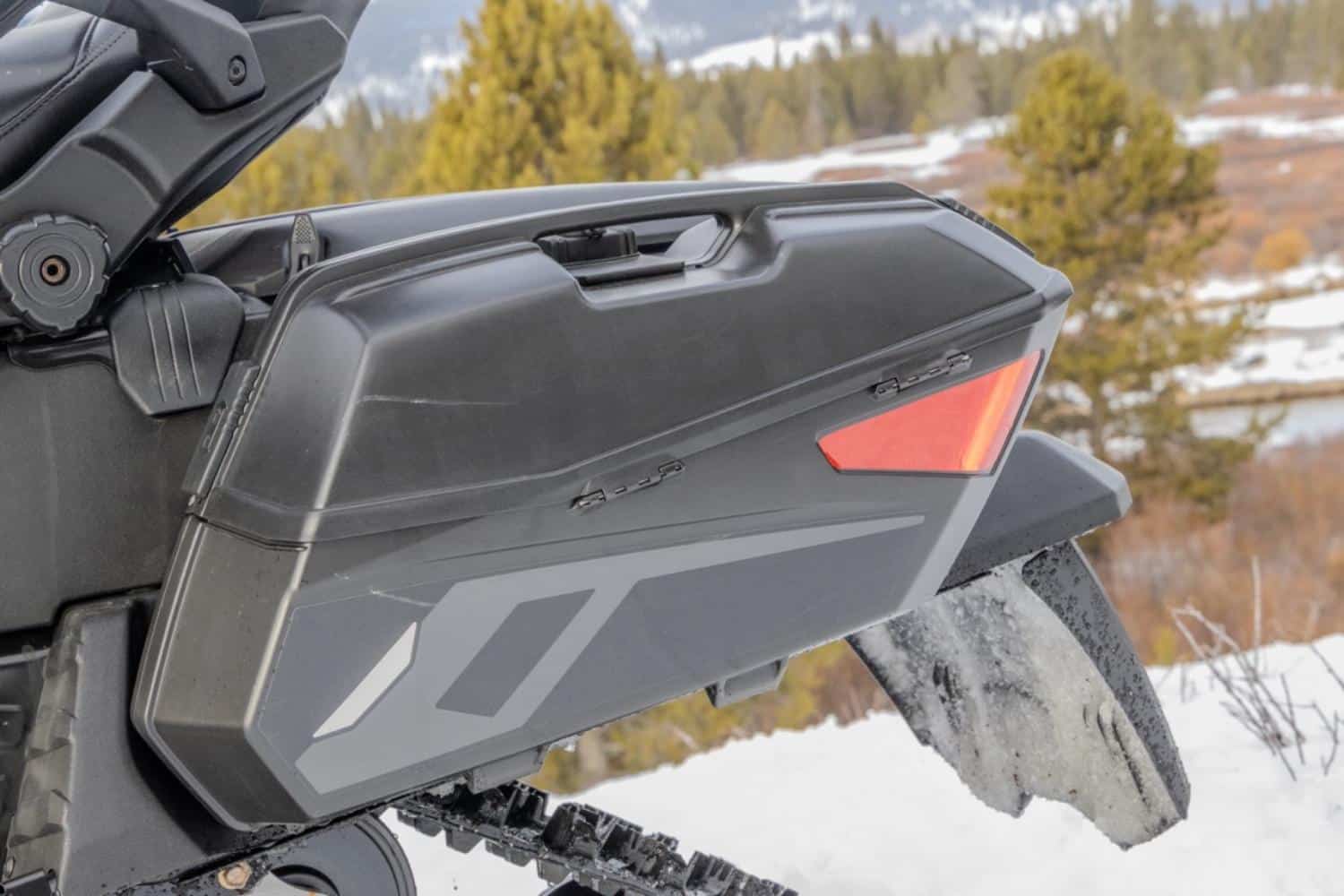 Gros plan de la valise latérale d’une motoneige Arctic Cat Pantera, montrant l’espace de rangement intégré et la partie arrière de la chenille dans un décor enneigé.