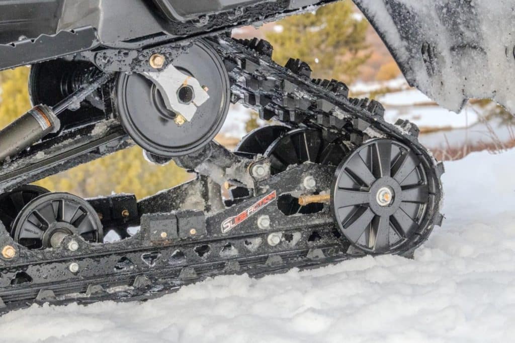 Gros plan du système de chenille et de la suspension arrière Slide-Action d’une motoneige Arctic Cat Pantera 9000, avec accumulation de neige sur les composants mécaniques.