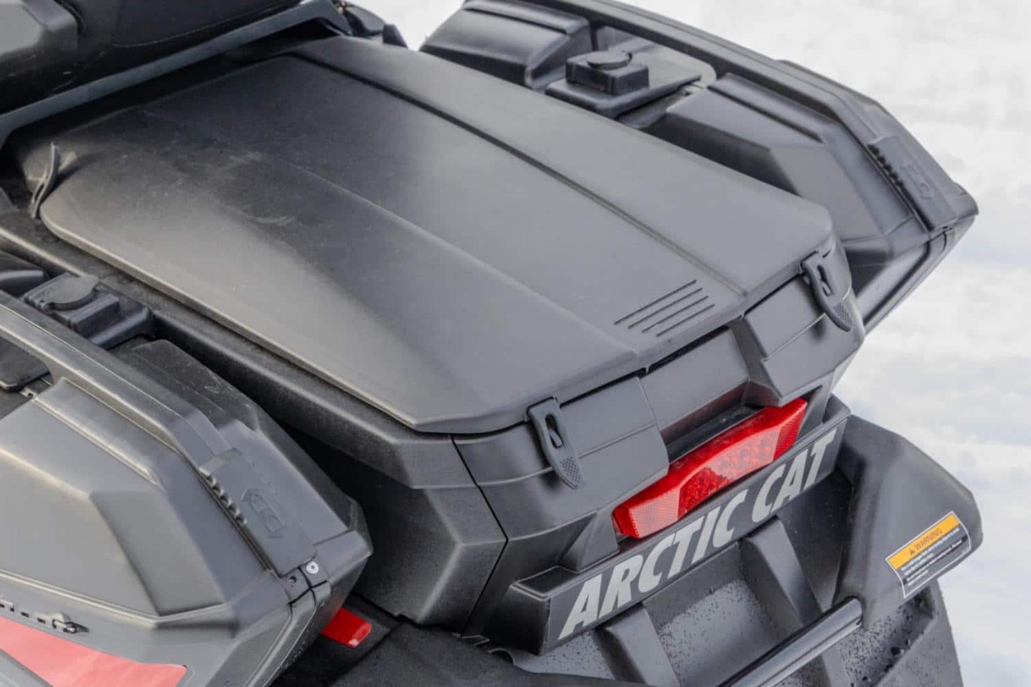 Vue rapprochée du coffre arrière et des compartiments de rangement d’une motoneige Arctic Cat Pantera, avec feu arrière intégré et finition noire sur fond enneigé.