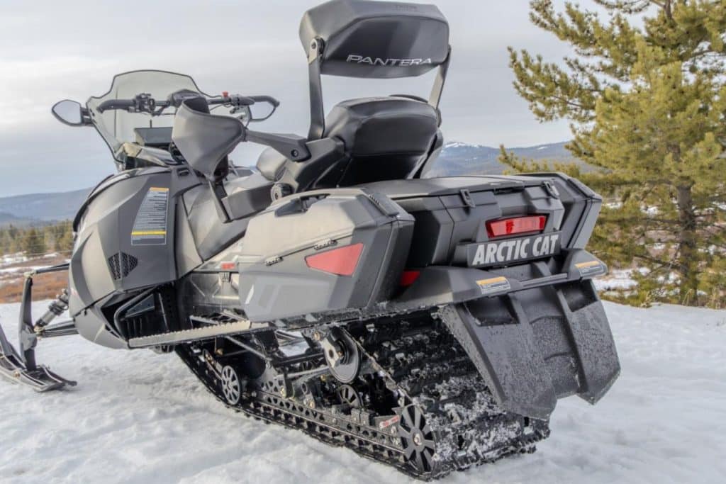 Vue arrière trois quarts d’une motoneige Arctic Cat Pantera stationnée sur la neige, avec siège passager, valises latérales et chenille arrière dans un paysage montagneux.