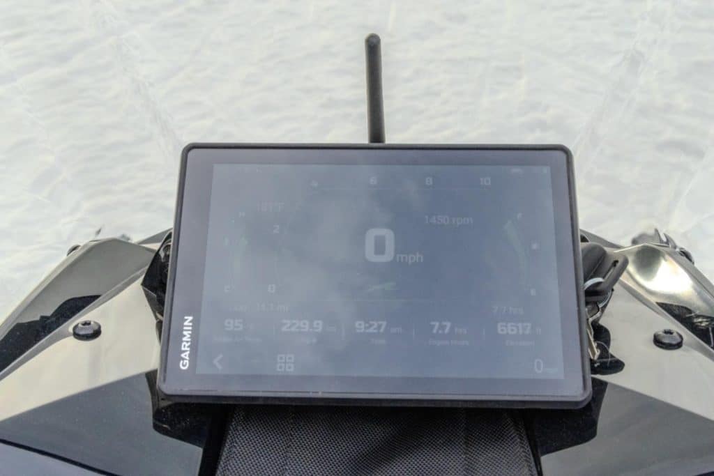 Vue du tableau de bord numérique Garmin installé sur une motoneige Arctic Cat Pantera, affichant les données de conduite et les informations moteur sur une piste enneigée.