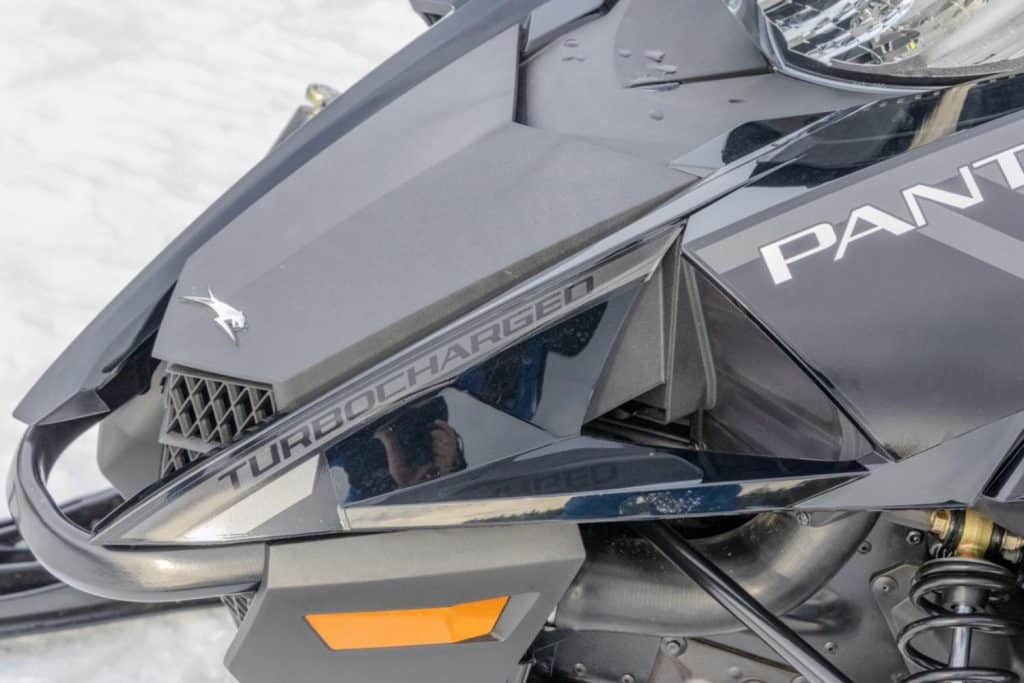Gros plan du carénage avant d’une motoneige Arctic Cat Pantera Turbocharged, montrant les détails du design, la suspension avant et les éléments de protection sur fond enneigé.